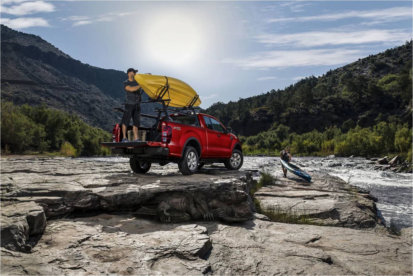 A Ford Ranger along a river with a man unloading a kayak from the back.