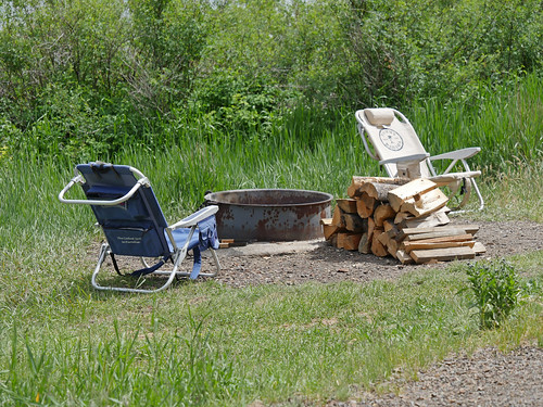 two lawn chairs around a fire ring with logs ready to burn