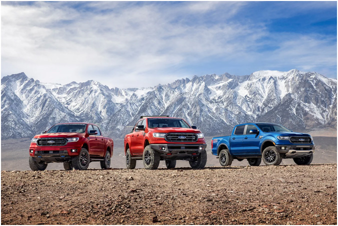 Two red Ford Rangers and a blue one parked on dirt with snow covered mountains in the background.