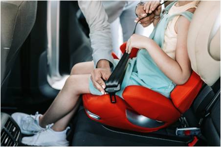 A child getting buckled in a dark orange car seat.