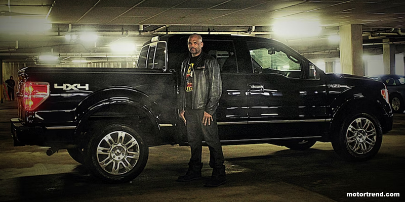 Man wearing black leather jacket standing in front of black Ford truck