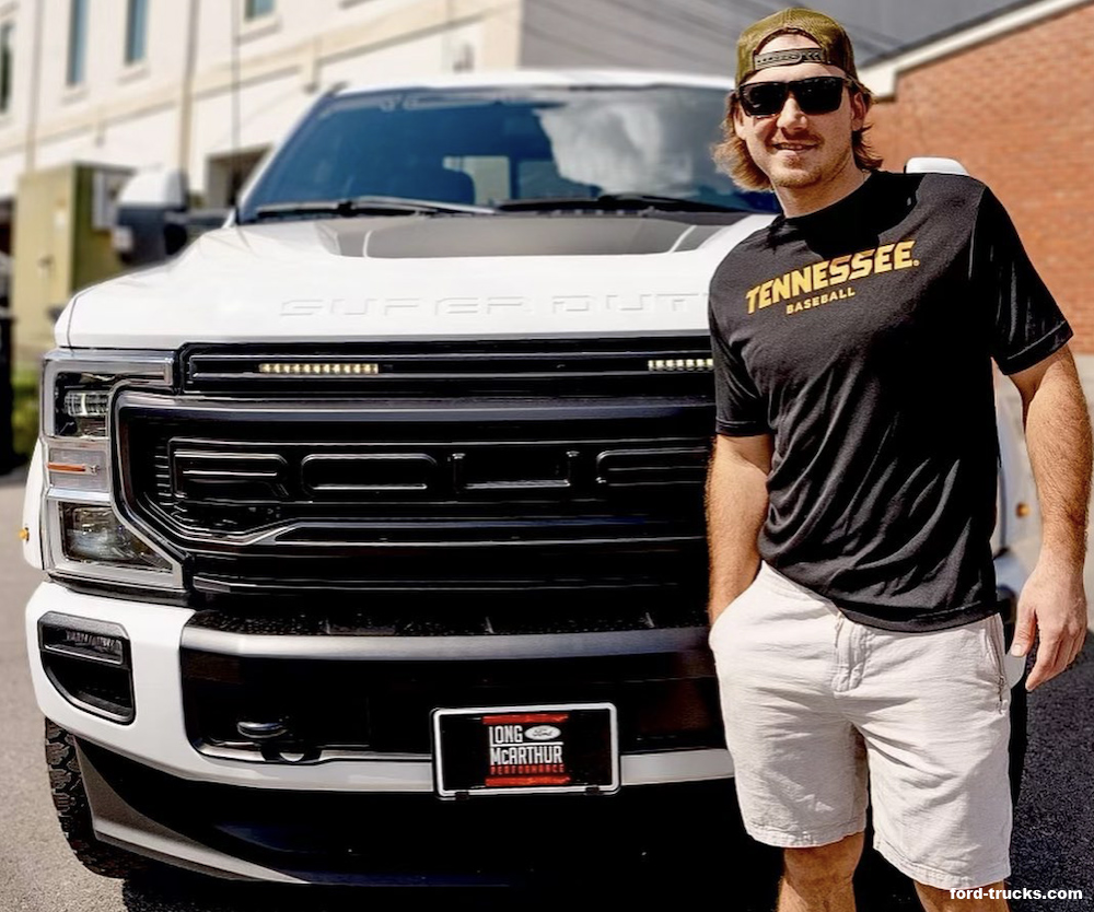 Man wearing black tee shirt and white shorts standing in front of white Ford truck